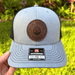 Gray and black SoCal Brewing Supply cap with a brown leather patch and Richardson logo, held against a grassy background.