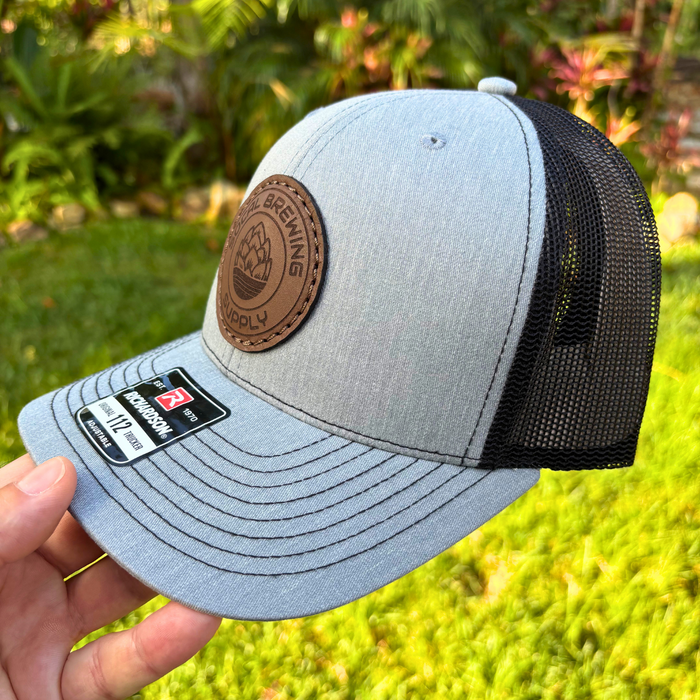 Gray cap with black mesh back held in front of a blurred green outdoor background
